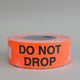 A roll of fluorescent red labels with the text 'DO NOT DROP' in black.